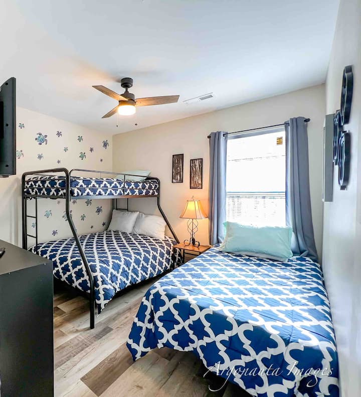 Kids room or bunk room with a ‘twin over full’ bunk bed and additional twin bed, black-out curtains, white noise machine, and a smart tv.