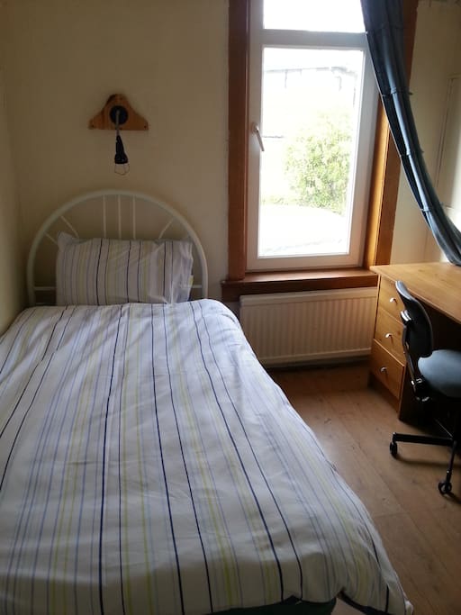 Single be room with a large window and a desk.