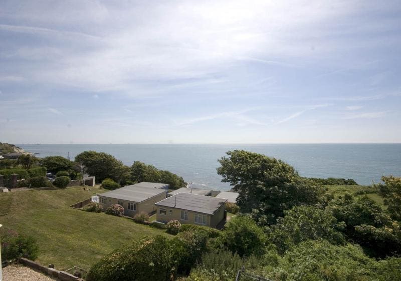 Views of the expansive sea stretch across the horizon, framed by lush greenery. A clear sky with soft clouds enhances the scenery, while the gentle waves can be seen lapping at the coastline in the distance.