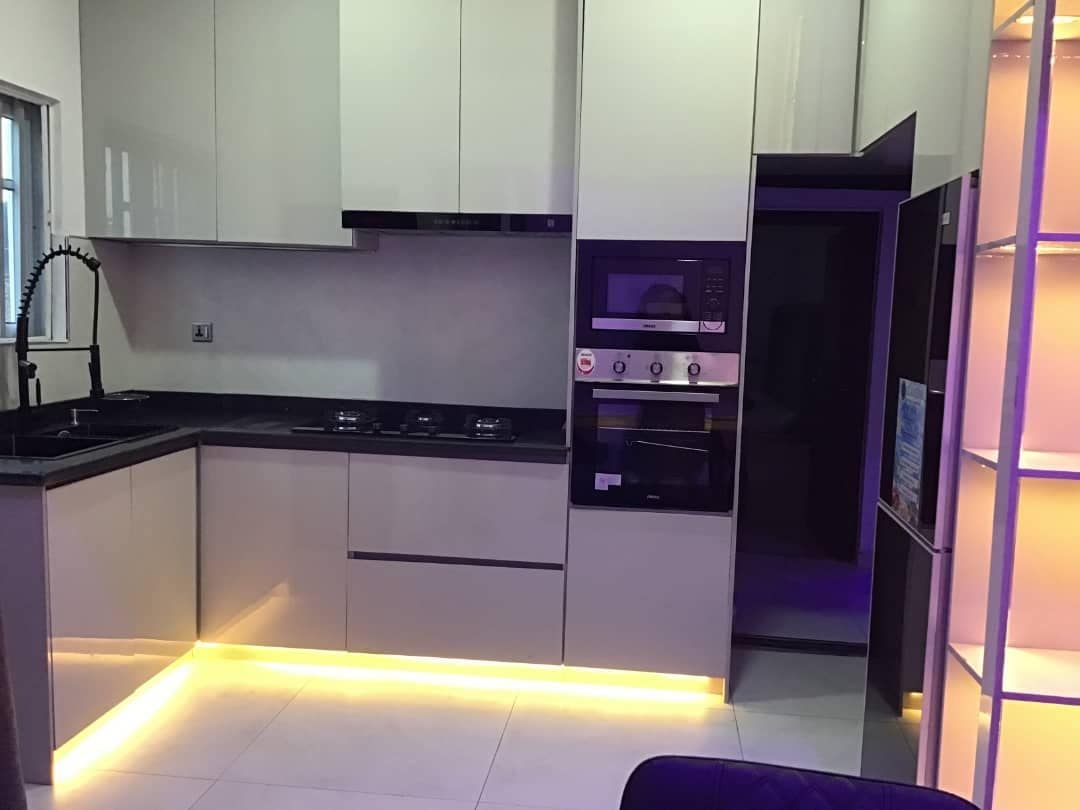 A modern kitchen features sleek cabinetry with a polished finish. Equipped with a gas cooktop, built-in oven, and a spacious refrigerator, the kitchen also includes under-cabinet lighting that casts a soft glow across the counter, enhancing the contemporary design.