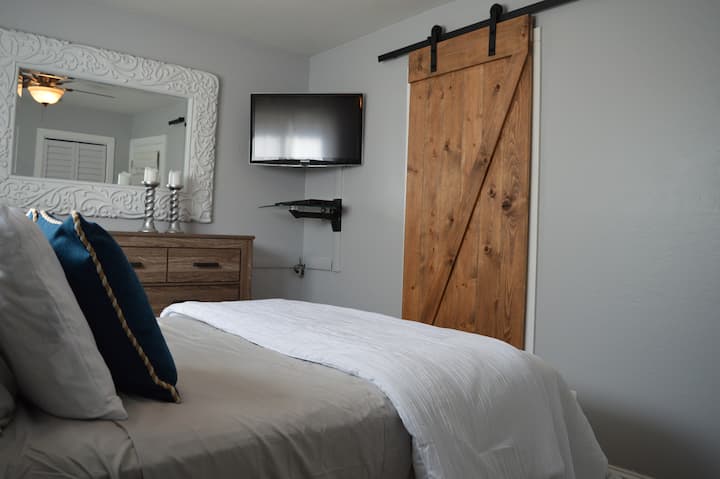 Dormitorio principal con cómoda grande, TV de 32pulgadas montada con reproductor de Blu-Ray y puerta corrediza de granero que conduce al baño privado.