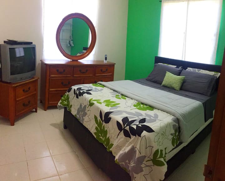 绿色房间/主卧配有一张1.8米宽双人床、梳妆台/镜子、电视/DVD播放器、衣柜、浴室和空调。