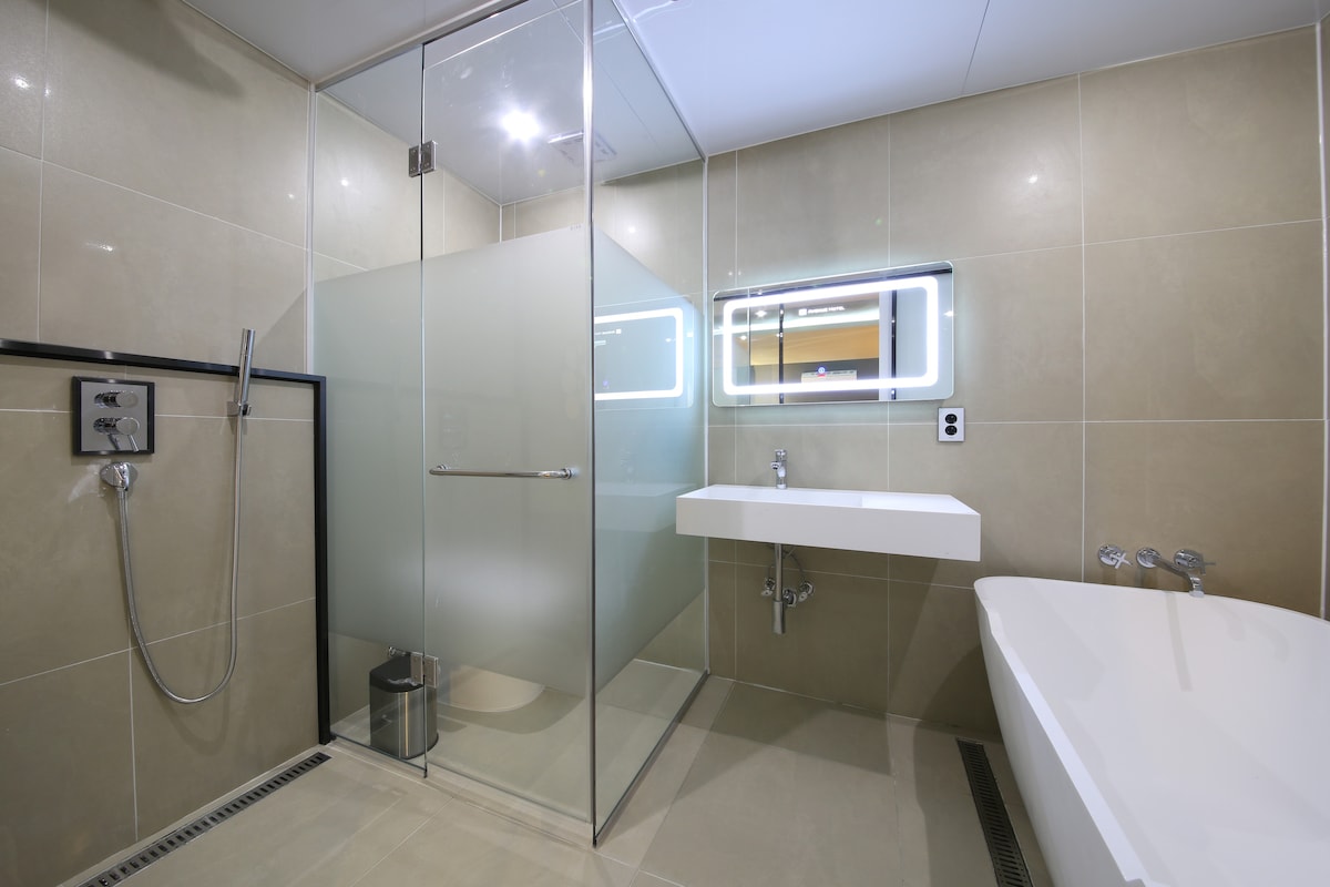 A modern bathroom features a spacious glass shower enclosure and a sleek white sink mounted on a light-colored wall. A backlit mirror adds brightness, while a standalone bathtub offers a relaxing option. Clean lines and neutral tones create a fresh and inviting space.