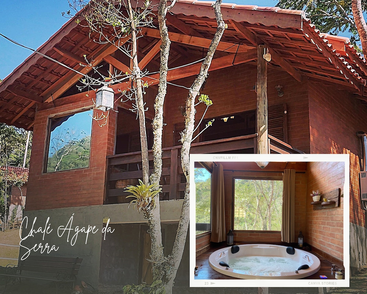 A charming chalet is set among trees, featuring a spacious outdoor area with rustic architecture. Inside, a large hydromassage tub is positioned by a window, offering views of the surrounding nature. Natural light enhances the warm tones throughout the space.