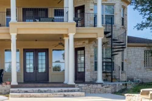 The exterior of the property showcases a welcoming entrance with double doors framed by large windows. A spiral staircase leads to the upper level, while a stone foundation enhances the structure's stability. The porch is adorned with white columns, providing a classic touch.