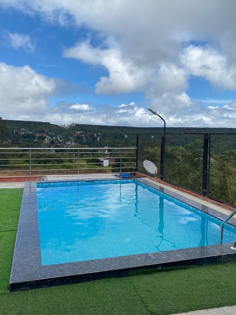 A private plunge pool is visible, surrounded by green grass and offering views of the mountains and landscape. The pool's clear water reflects the sky, while a railing provides safety. Nearby, a light fixture and satellite dish are positioned for convenience.