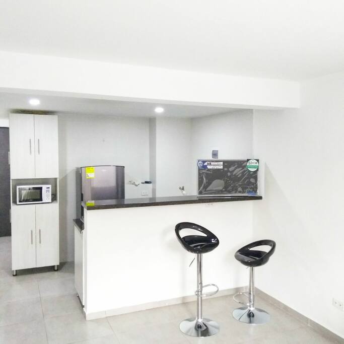 Cocina con red de gas, nevera, microondas, gabinetes y barra americana.