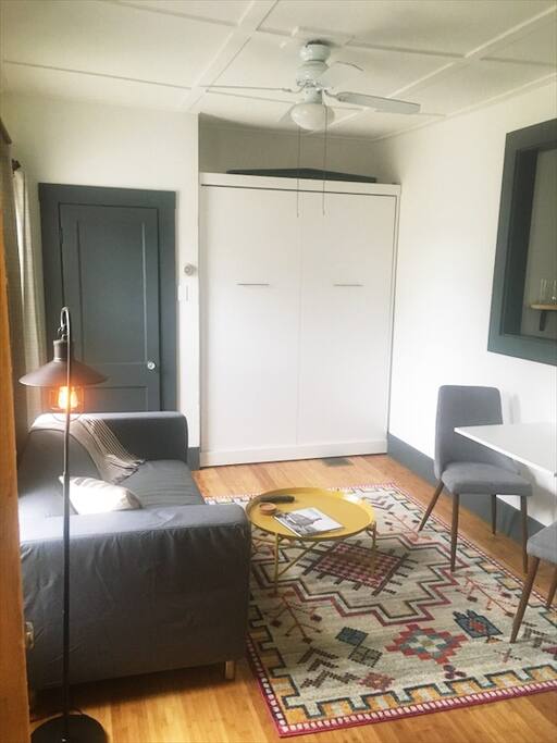 Living room includes brand new love seat, throw blanket, coffee table, dining table/desk for two and murphy bed.