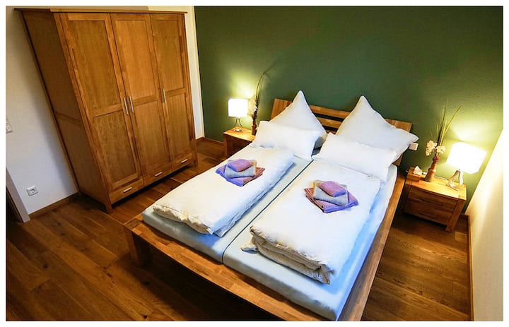 Le vert intense combiné au chaud brun des meubles en chêne massif dans la chambre « Sepp » reflète la beauté des forêts naturelles. La chambre de 14 m ² est située dans un endroit calme par rapport au jardin et jouxte directement la salle de bain confortable. La température ambiante peut être parfaitement adaptée à vos besoins individuels à l'aide du chauffage au sol en parquet en bois véritable.