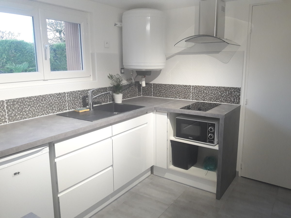The kitchen features sleek white cabinetry and a gray countertop. A modern stove and microwave are integrated into the design, with a compact sink positioned beneath a window. The backsplash is adorned with decorative tiles, and a small potted plant adds a touch of greenery.