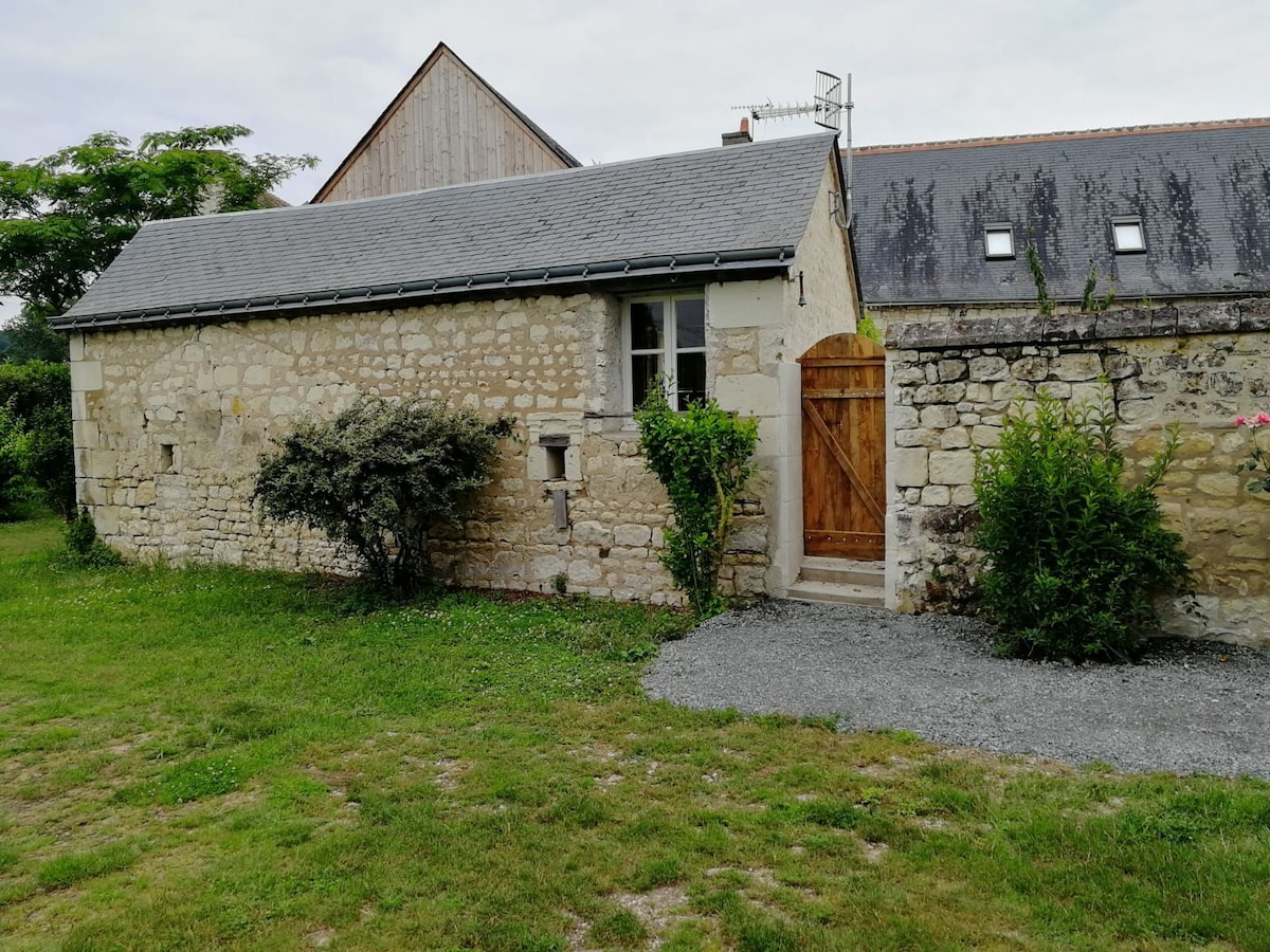 An exterior view of a rustic stone building is presented, featuring a wooden door framed by natural greenery. The surrounding grassy area is well-maintained, with gravel path leading to the entrance. A peaceful and inviting atmosphere is created by the serene landscape.
