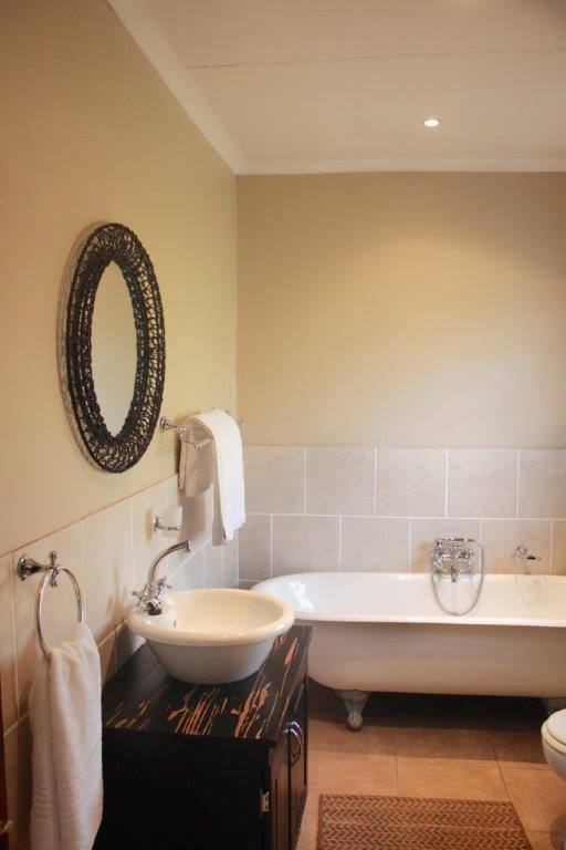 The bathroom features a freestanding bathtub with a chrome faucet, accompanied by a modern circular mirror. A stylish, dark wood vanity is positioned beneath an elegant wash basin. White towels are neatly hung for convenience, enhancing the room's clean design.
