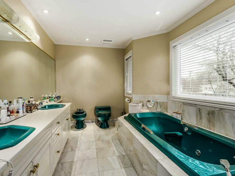 The spacious bathroom features dual sinks with green countertops and cabinetry. A large bathtub is positioned against a natural stone wall. Additional fixtures include a toilet and complimentary amenities. Natural light filters in through multiple windows, enhancing the room's serene atmosphere.