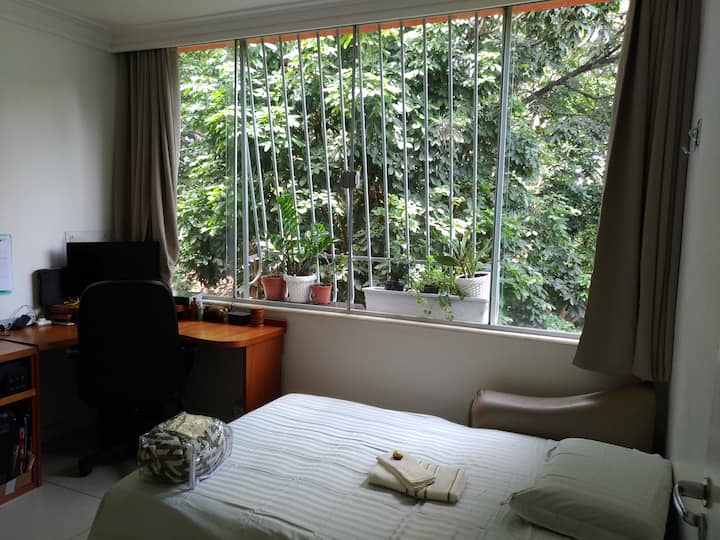 Chambre avec canapé-lit, grande fenêtre avec rideau occultant, bureau et chaise confortable.