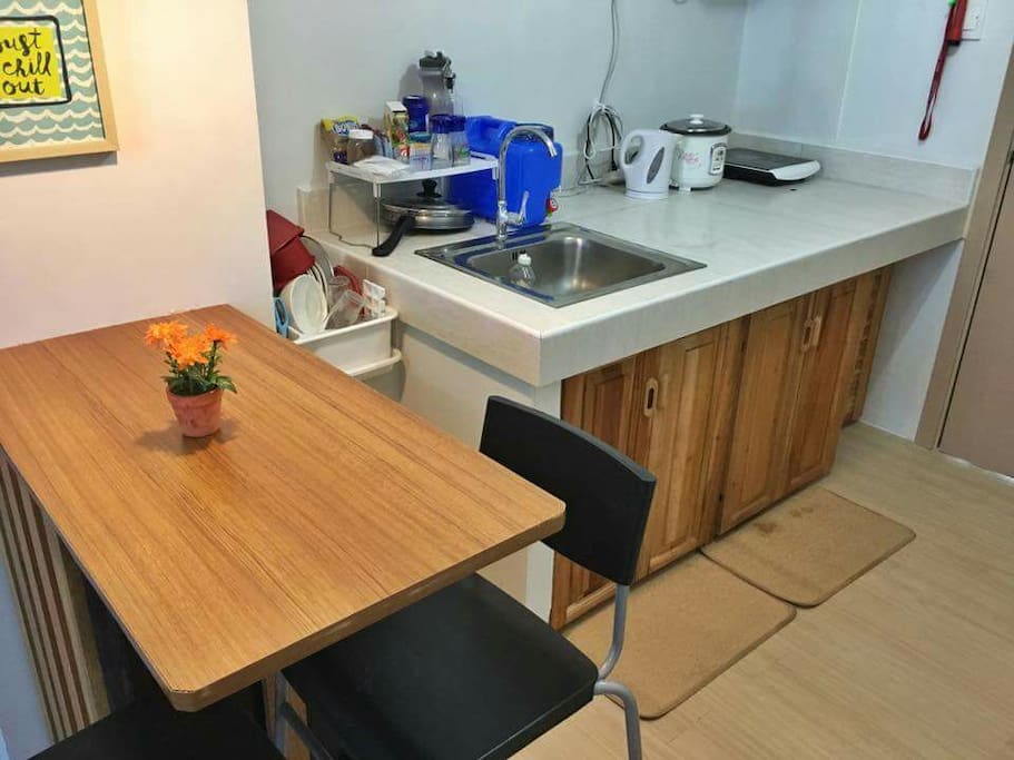 Dining Table w/ fridge under. Kitchen w/ rice cooker, stove, electric kettle and basic kitchen utensils.