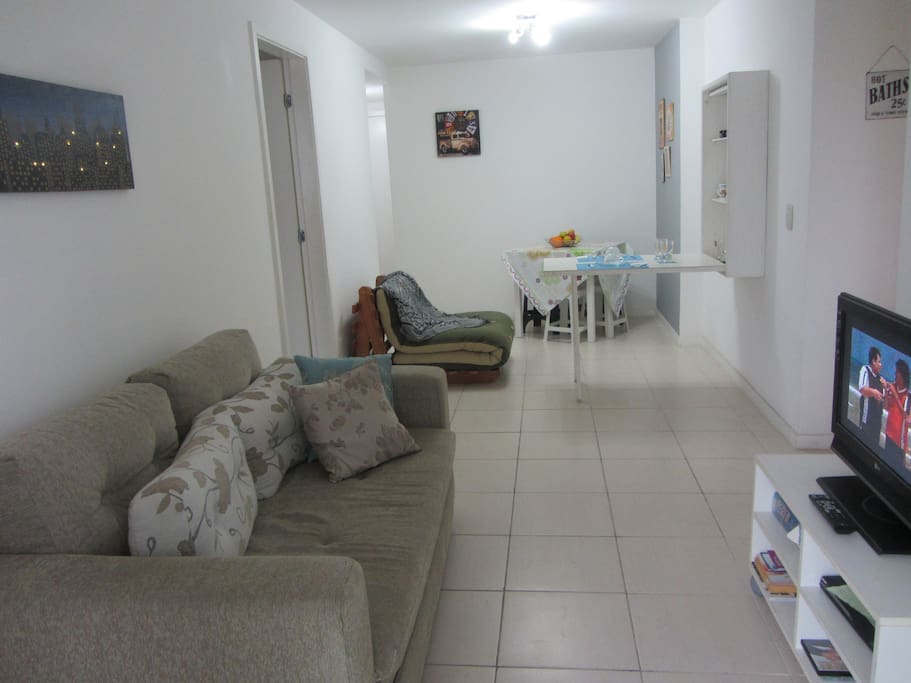 Sala com sofá-cama, futton, tv, mesa, e mesa-bar aberta