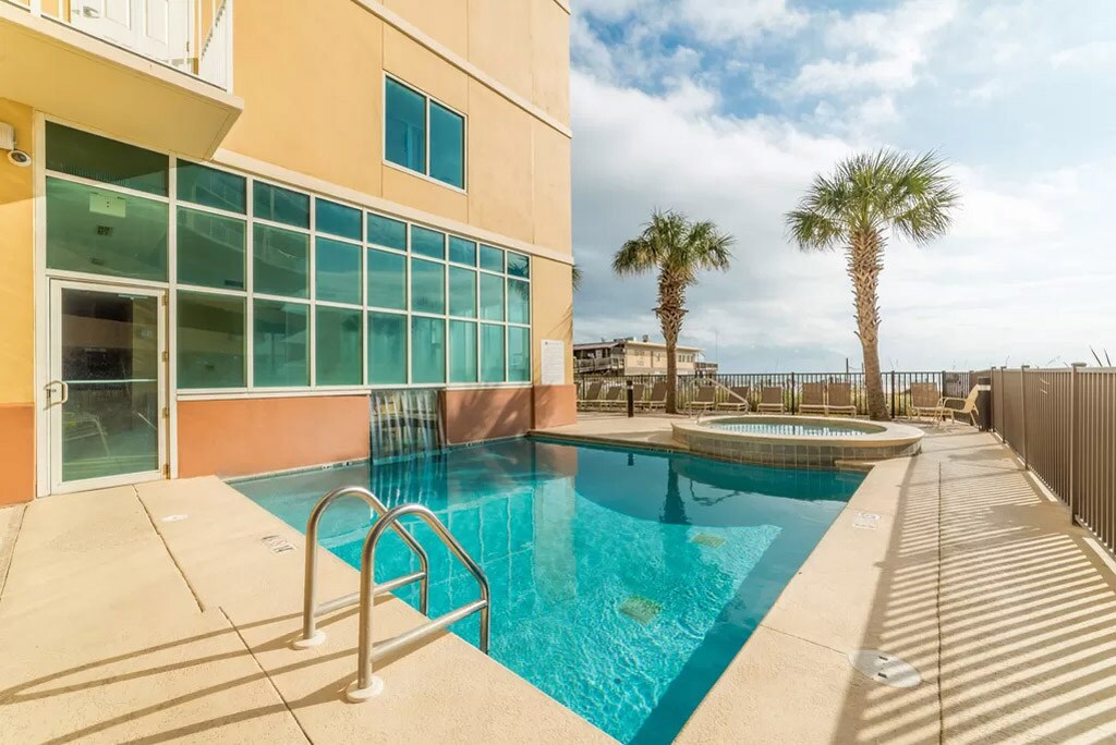 An outdoor area features a heated pool and a hot tub, surrounded by palm trees. Large windows provide views of the beach, while the pool deck offers ample space for lounging. The clear water reflects the sky, inviting relaxation and enjoyment.
