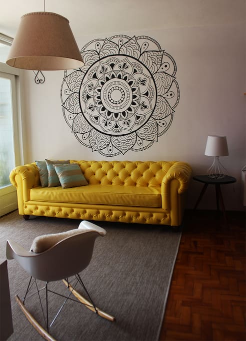 A nossa sala de estar tem uma mandala desenhada na parede, você pode meditar bem cedinho pela manhã ou no fim da noite, ou apenas olhar pra ela por alguns minutos, respirar fundo e mentalizar coisas boas. E sim, esse sofá é mesmo um espetáculo!!
