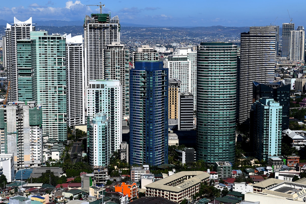 A panoramic view of a modern city skyline, featuring a variety of high-rise buildings and distinctive architectural designs. Various shades of blue and grey dominate the structures, while greenery can be seen interspersed among the urban landscape. The scene reflects the vibrant character of the city.