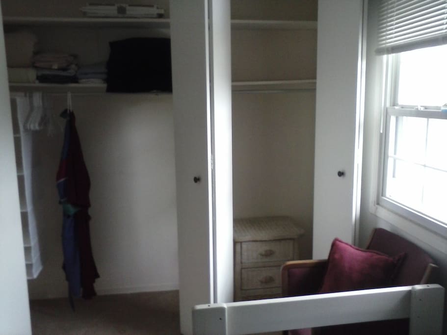 large closet with shelves, small dresser, chair, large window.