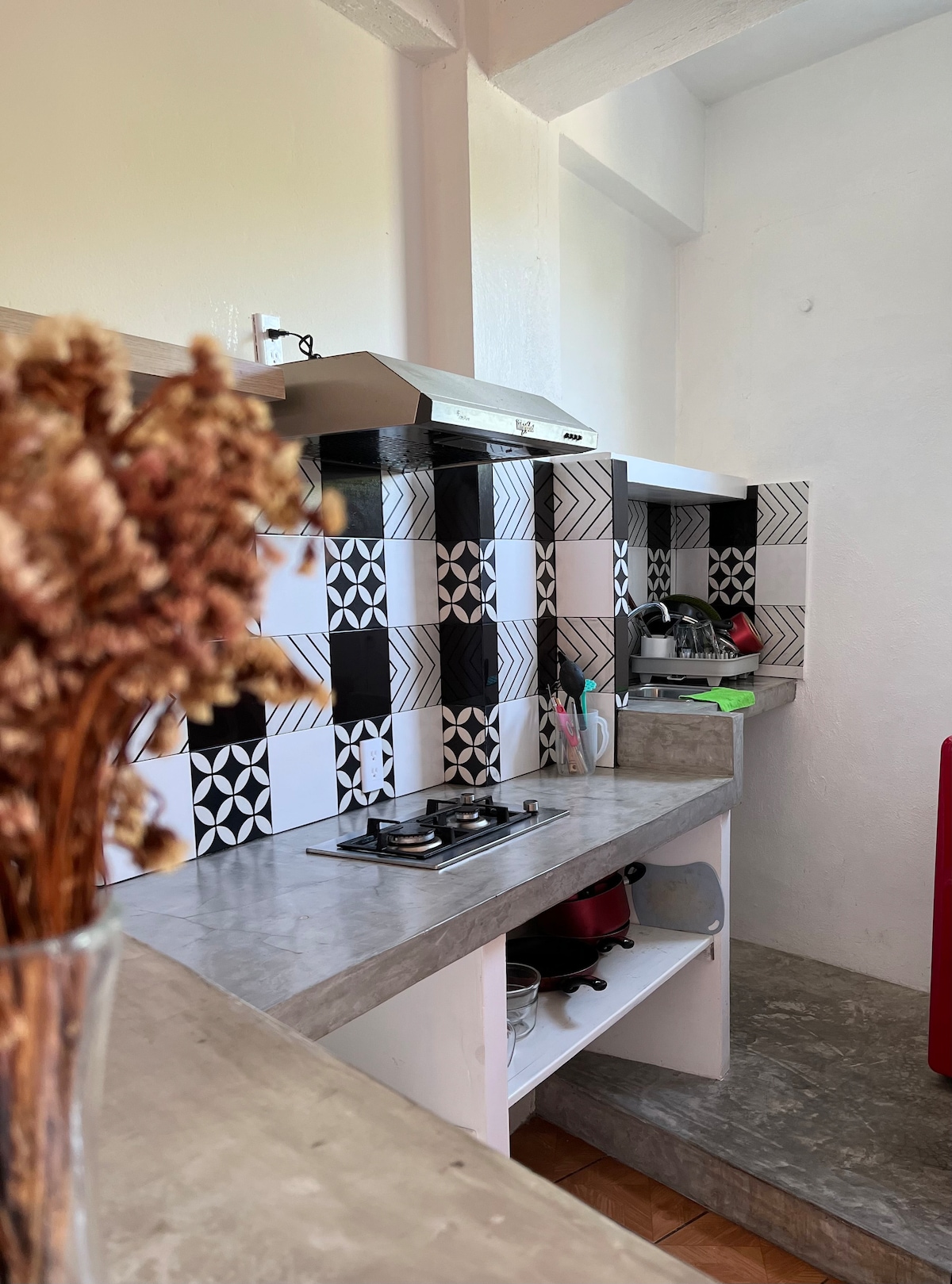 A kitchen area features modern appliances and a stylish tile backsplash in black and white patterns. Counter space is provided for food preparation, with a stove and utensils within easy reach. Light neutral tones create a clean and functional atmosphere.