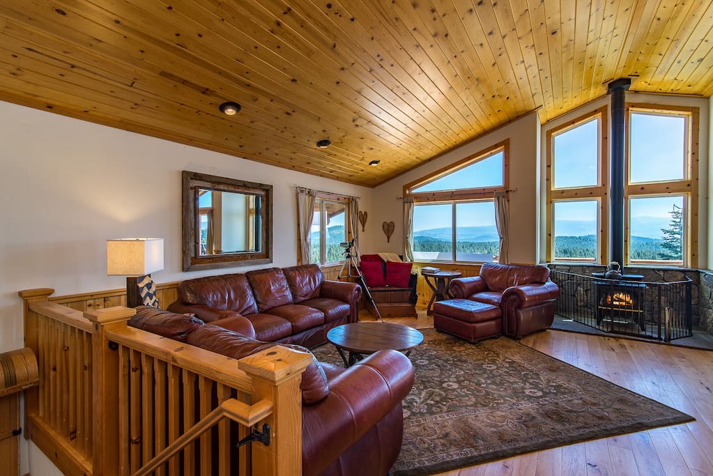 The main living room boasts leather furniture, sweeping views, and a wood stove