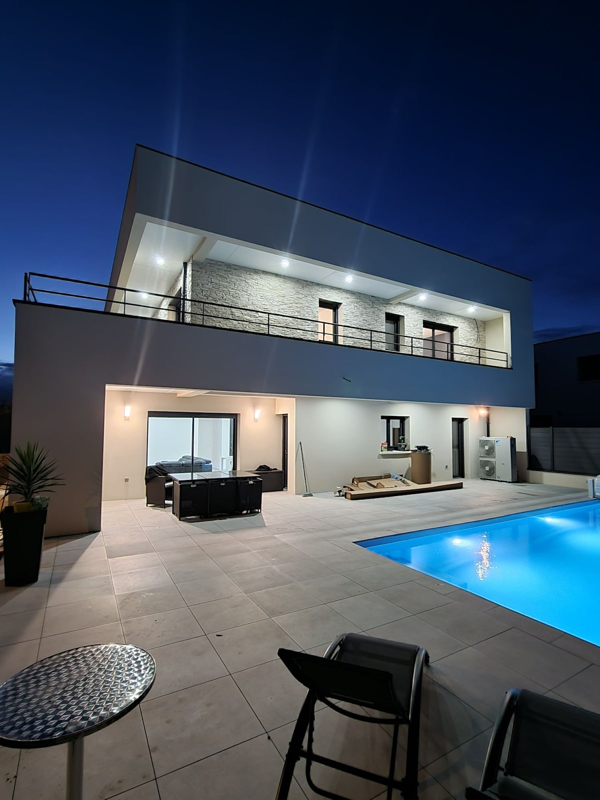 A modern villa is displayed at dusk, featuring a spacious terrace with outdoor seating arrangements and a private pool. Soft lighting illuminates the façade, highlighting the architectural details. The open floor plan connects the indoor and outdoor spaces, creating a seamless ambiance for relaxation.