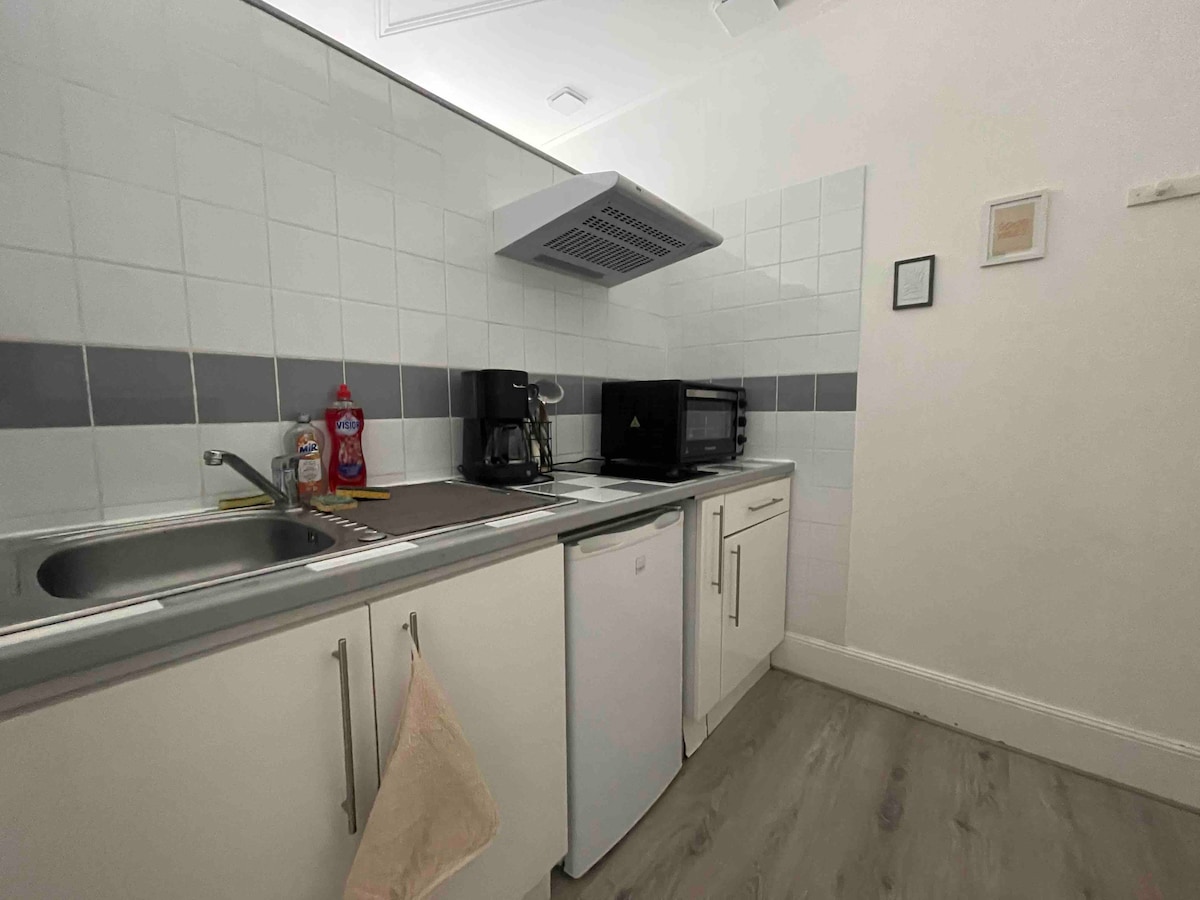 An equipped kitchen area is visible, featuring a sink, a refrigerator, a coffee maker, and a microwave. The countertops are neatly arranged with kitchen essentials, and tiled walls provide a clean and functional design. A towel hangs from a cabinet handle for convenience.