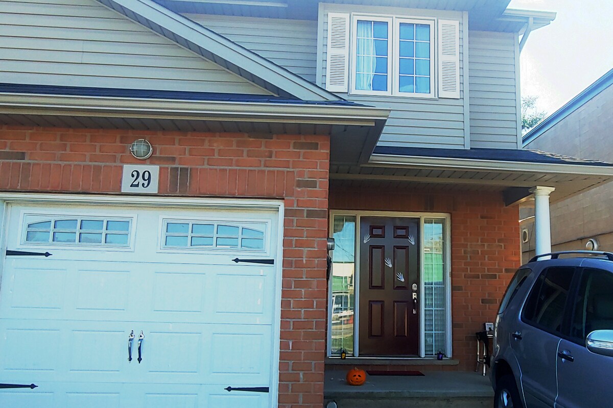 The exterior view of a two-story home showcases a brick facade with a large garage door and a welcoming front door. A decorative pumpkin is placed on the steps, and a vehicle is parked in the driveway. Natural light highlights the windows above the entrance.
