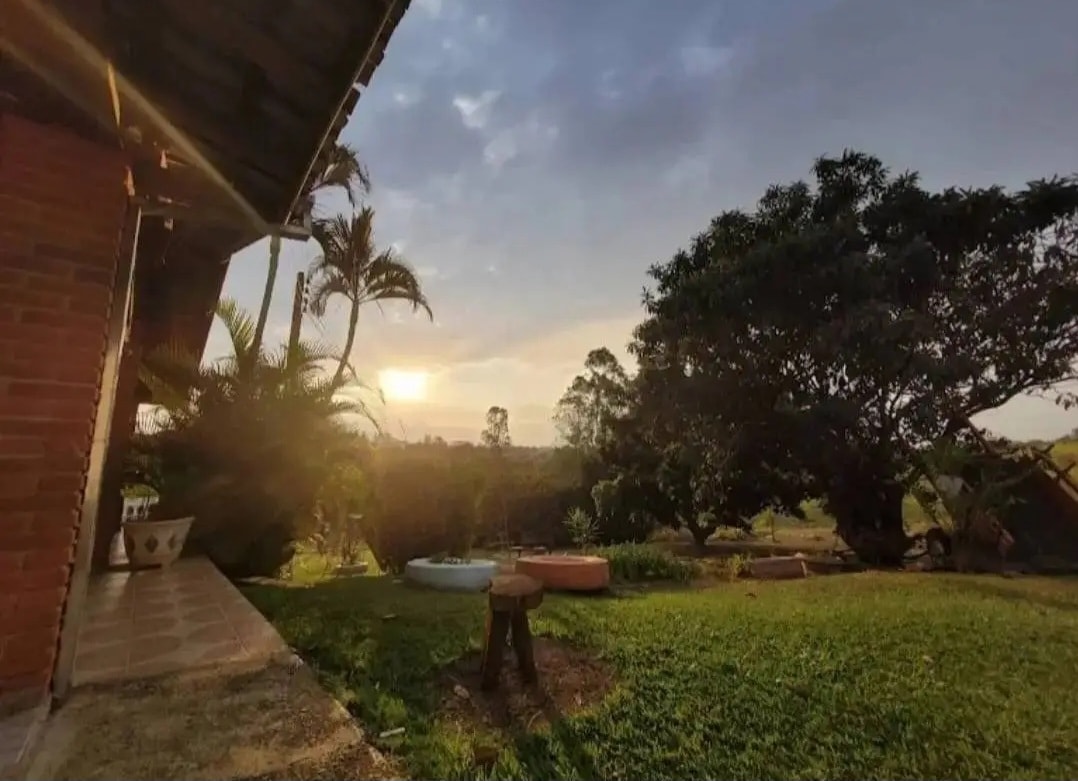 The outdoor area features well-maintained grass and scattered trees, with a view of a sunset illuminating the horizon. An inviting atmosphere is created by the presence of lounge spaces and a paved path leading to the main structure.