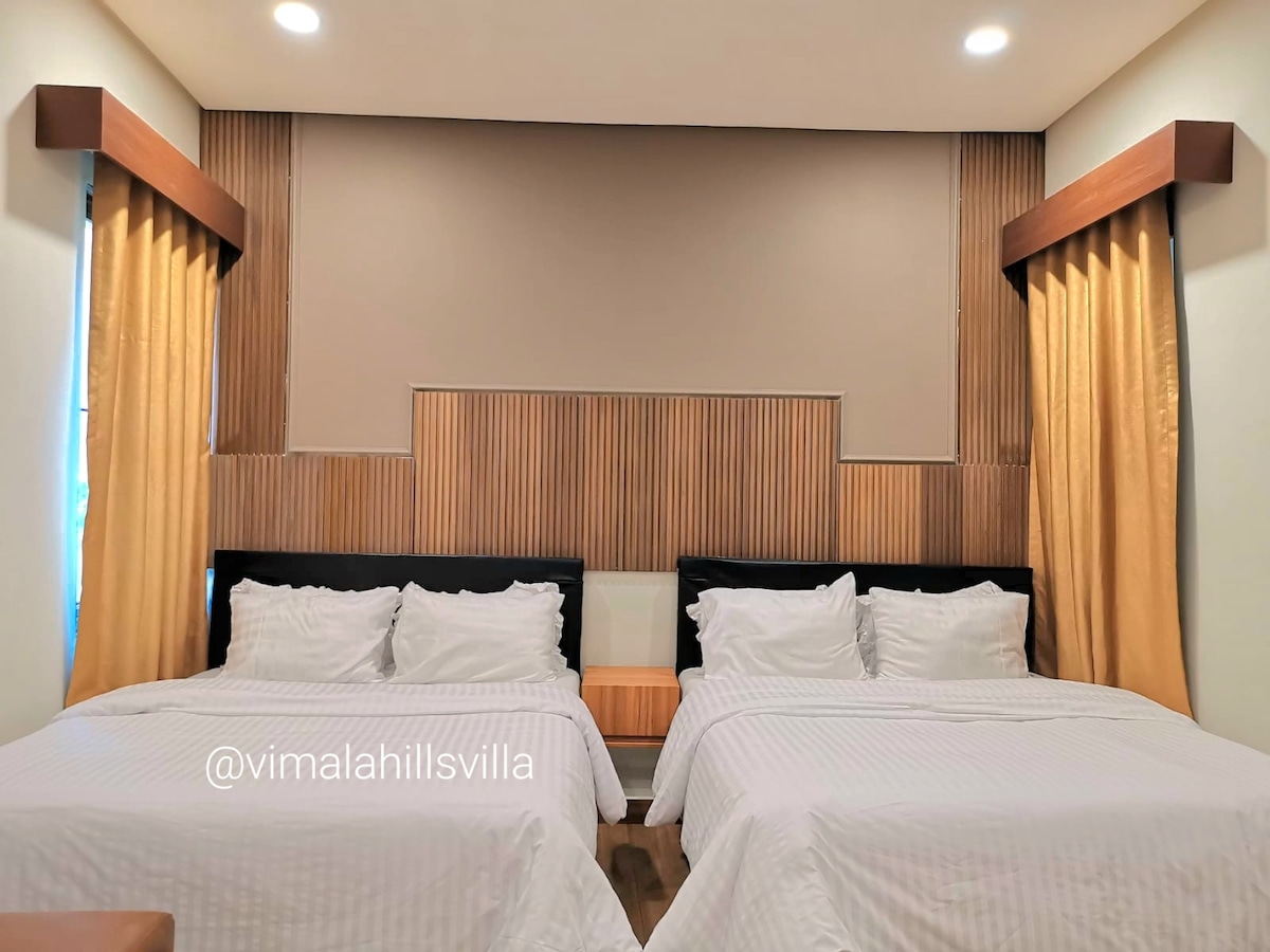 The master bedroom features two spacious queen-size beds with crisp white linens. Soft yellow curtains frame the windows, complementing the wooden paneling on the walls. A cozy seating area is positioned at the foot of the beds, enhancing the room's inviting atmosphere.