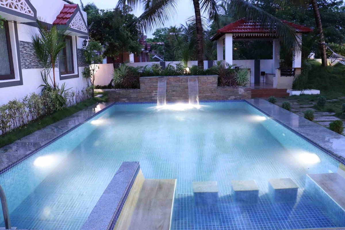 A serene private pool is showcased, featuring gentle water features and softly illuminated lighting. The surrounding area is landscaped with lush greenery, while a gazebo stands in the background, emphasizing the tranquil outdoor setting.