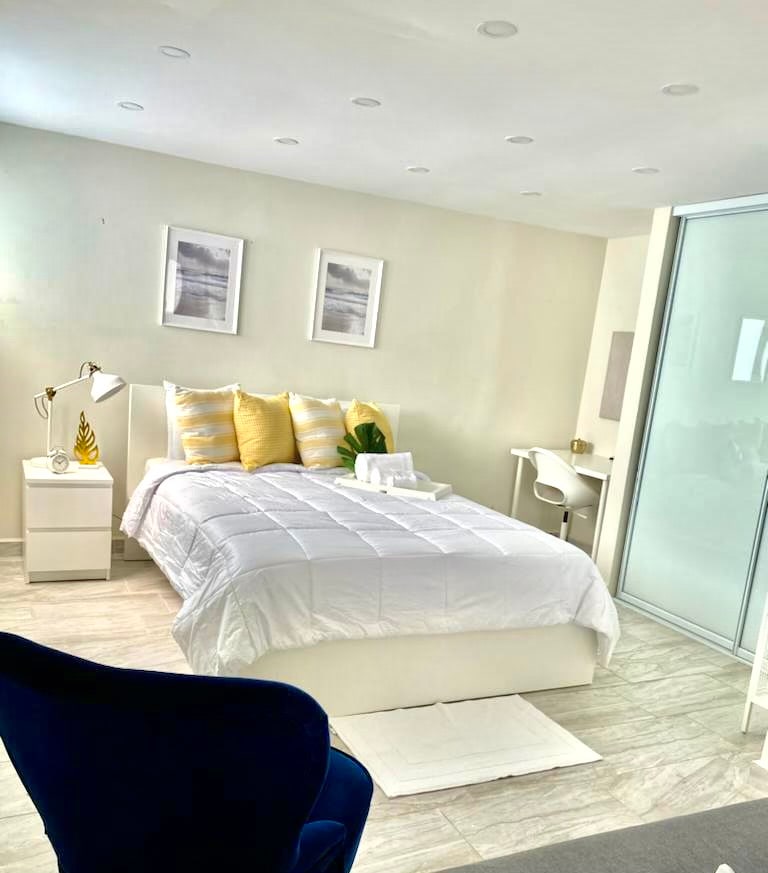 Chumba kilicho na mwangaza wa kutosha chenye kitanda kizuri, meza ya kulala yenye taa, dawati, kioo cha ukuta na kiti cha kupumzikia.