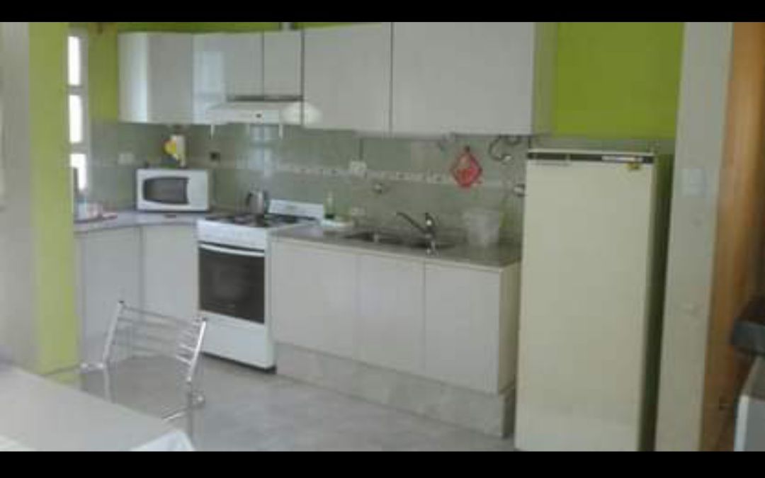 The kitchen features modern cabinetry and appliances, including a refrigerator and an oven. A microwave is placed on the counter, while a sink is integrated into the countertop. The vibrant green wall adds a touch of color to the space.