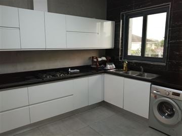 A modern kitchen features sleek white cabinetry and a black countertop. A gas stove is positioned on the left, while a sink with a window above it allows natural light to fill the space. A washing machine is located on the far right.