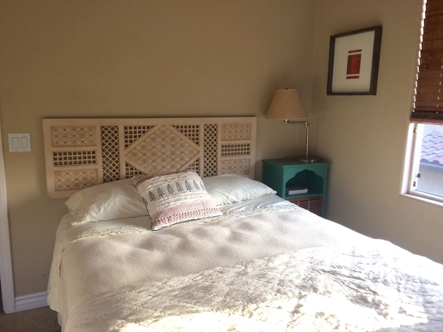 Guest room. Comfy queen bed, end table and lamp. To the left is a large closet with iron, ironing board and mirror.
