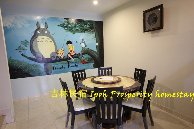 A dining area features a round table surrounded by black chairs. A vibrant mural depicting friendly animated characters and a forest scene adds a whimsical touch to the space. Soft lighting highlights the clean lines of the furniture and the light-colored tiled floor.