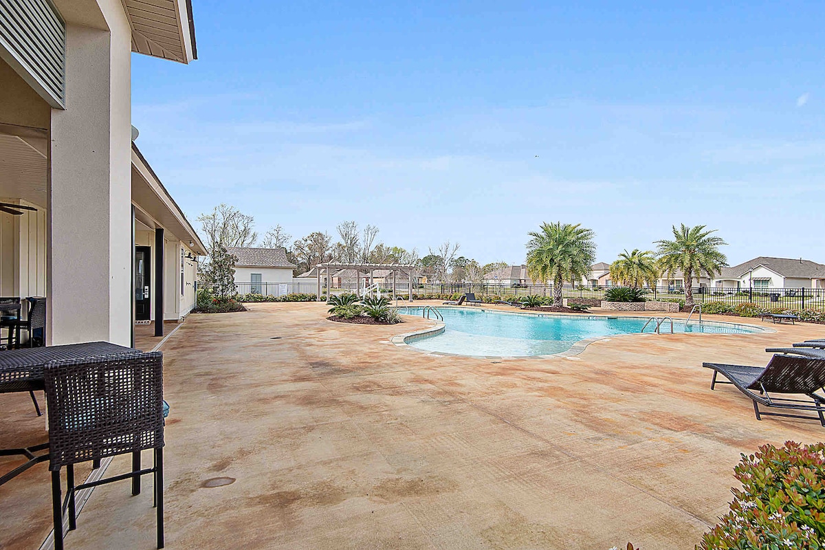 The outdoor area presents a spacious pool surrounded by a sun deck, complete with lounge chairs. Lush palm trees and well-maintained landscaping frame the scene, offering an inviting view of the clubhouse and the surrounding neighborhood.