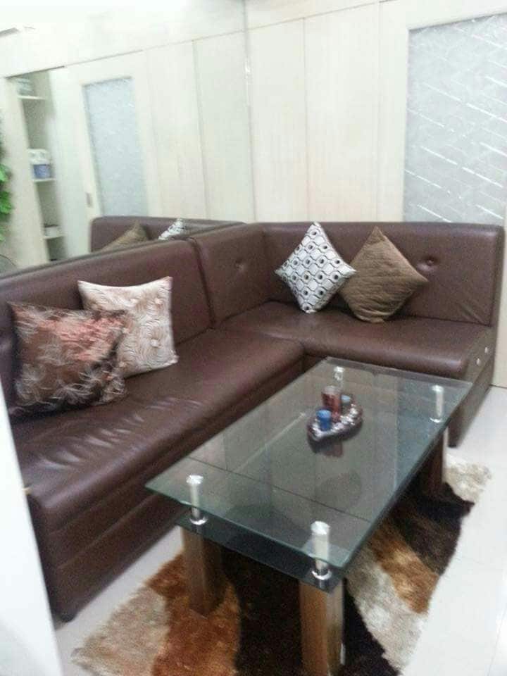 A modern seating area is equipped with a brown sectional sofa adorned with patterned cushions. A glass coffee table sits atop a soft area rug, complemented by decorative items. The surrounding walls are lined with mirrors, enhancing the space's openness.