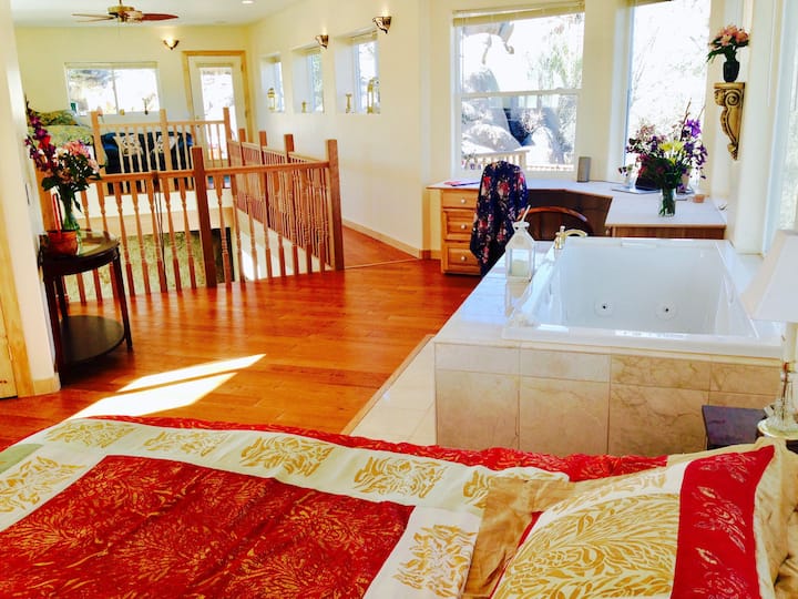 The majestic bedroom's king bed awaits you beside the marbled whirlpool tub. Notice the double executive desk and walkway above the cave living room to the loft featuring a couch and raised queen bed with custom suitcase storage and shelves below it.