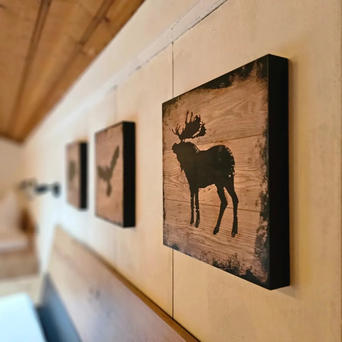 Three wooden wall art pieces feature silhouettes of woodland animals, including a moose, against a light wooden background. The pieces are arranged in a line, adding a rustic charm to the room's decor.