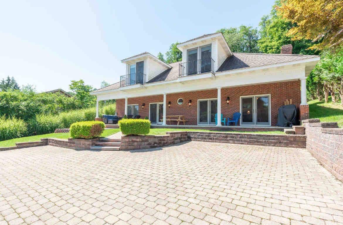 The exterior of the lodge features a brick facade with a spacious patio area, outlined by flower beds. Balconies are visible above, with seating options arranged on the patio and greenery surrounding the yard. A propane grill is positioned near the entrance.