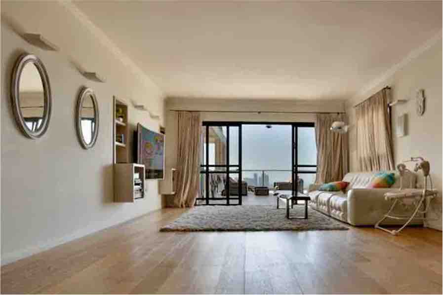 A spacious living area features a comfortable white sofa and a modern coffee table. Two circular mirrors are mounted on the wall, reflecting light. Floor-to-ceiling glass doors offer access to the terrace, while a large area rug enhances the floor's overall warmth.