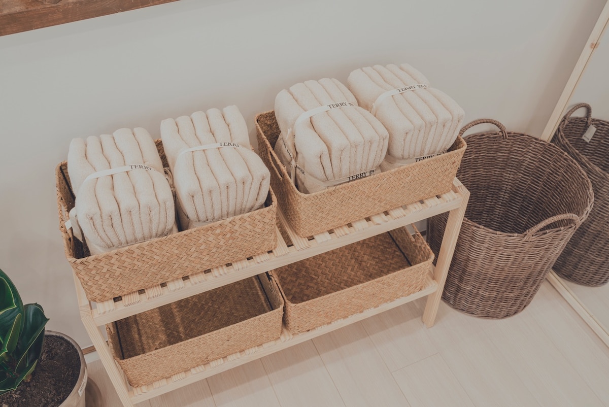 Neatly arranged towels are displayed in woven baskets on a wooden shelf. A spacious, empty shelf is present below, accompanied by additional wicker baskets, creating an organized and functional storage area.
