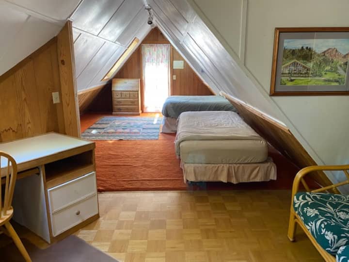 楼上阁楼。双人床、两张单人床、起居区、天窗下的书桌。  