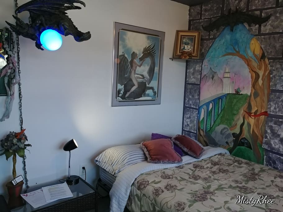 Dragon room double bed with lots of pillows, bedside table and lamp, with lots of dragon decor.