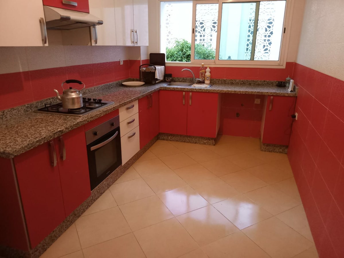 A modern kitchen features sleek cabinets in vibrant red and white. A spacious countertop is complemented by stainless steel appliances, including a gas stove and oven. Natural light fills the room through a large window overlooking leafy greenery.