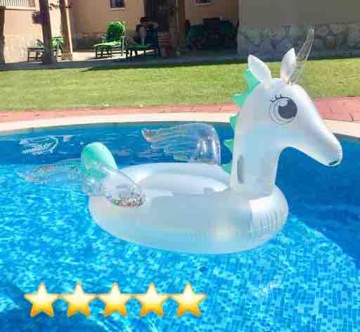 A whimsical unicorn float is positioned in a sparkling blue pool. Its bright white surface is complemented by colorful details, including a mane and wings. The surrounding area features a manicured grass edge, enhancing the inviting atmosphere of the private pool setting.