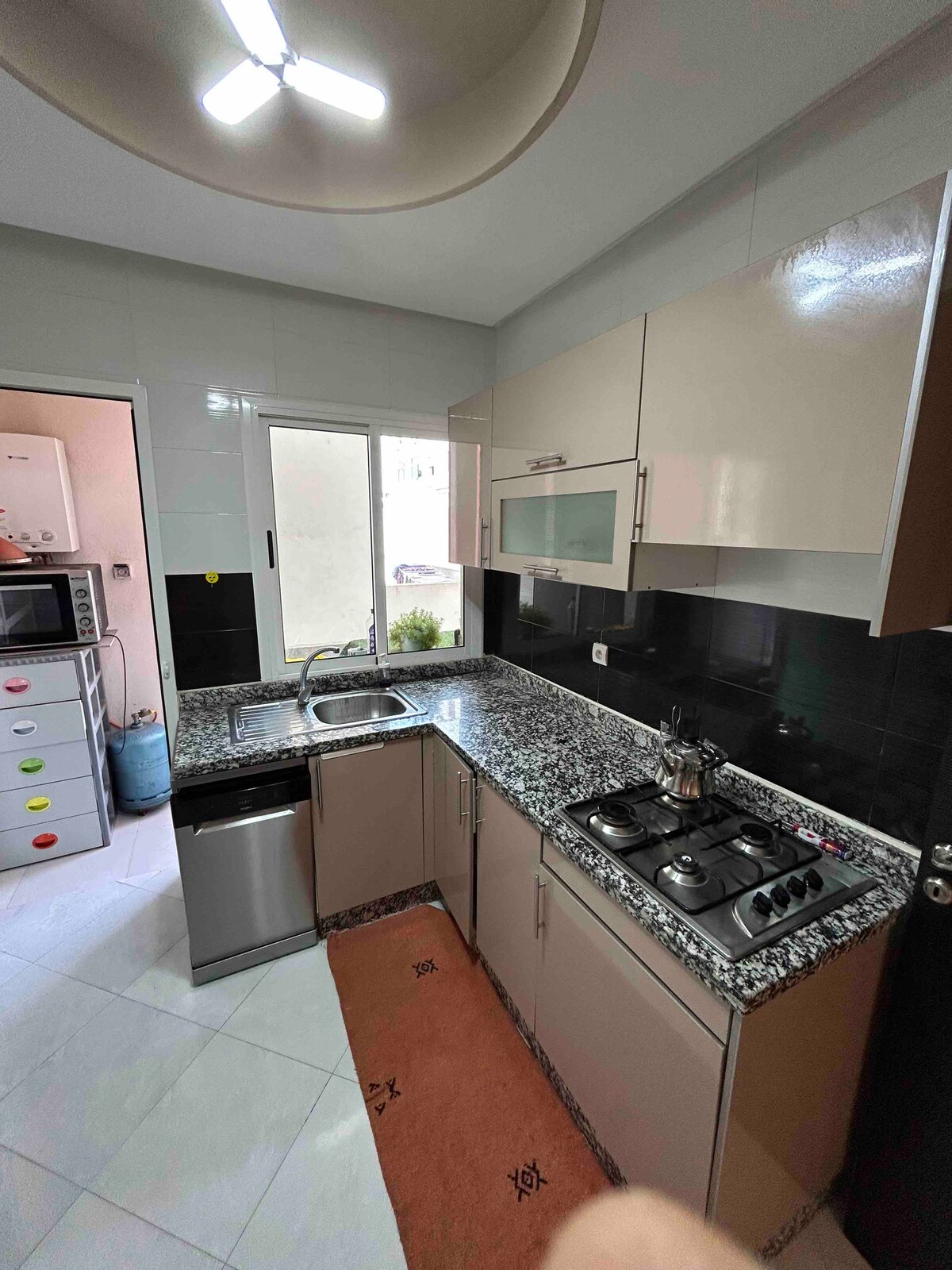 The kitchen features modern cabinetry with a combination of light and dark finishes. A granite countertop is complemented by a stainless-steel sink and a gas stove. Natural light is provided through a nearby window, offering a functional and inviting cooking space.