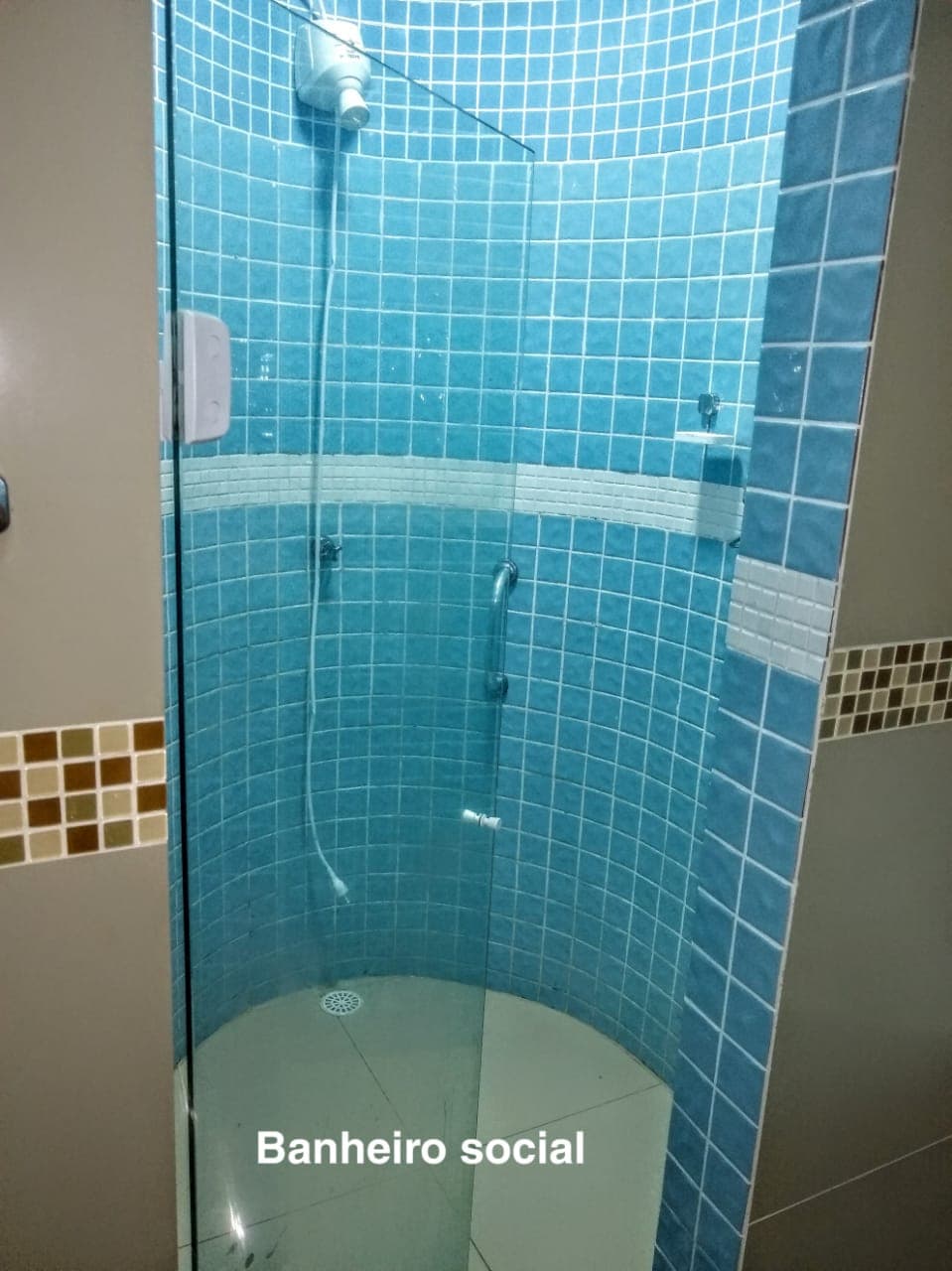 A modern bathroom is showcased with turquoise tiled walls and a rounded glass shower enclosure. The shower features a sleek faucet and a handheld showerhead. The floor is tiled in a light neutral color, creating a cohesive and clean appearance.
